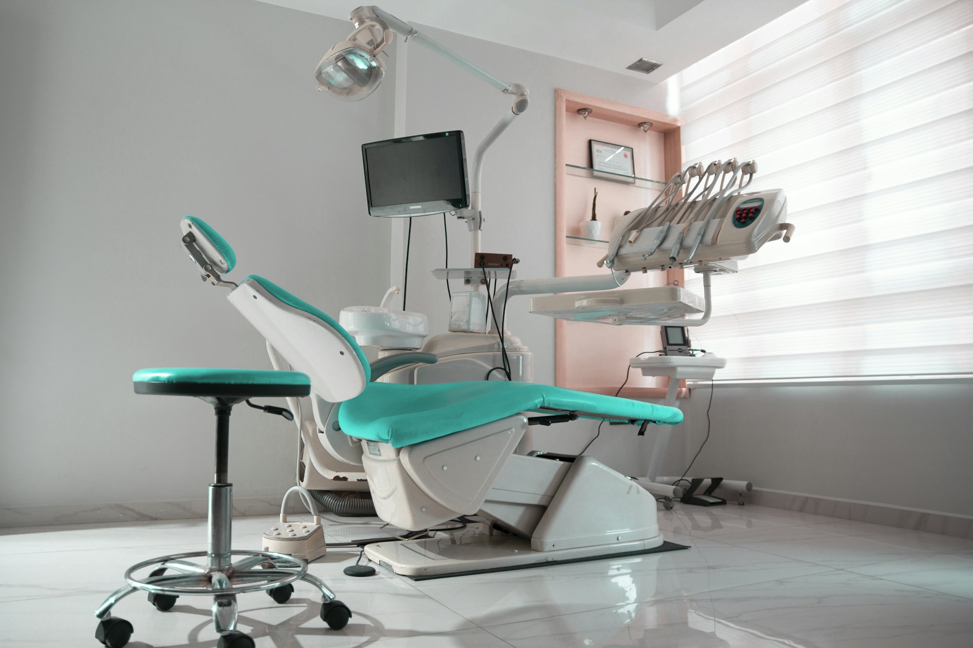 A bright, modern treatment room with a teal dental chair